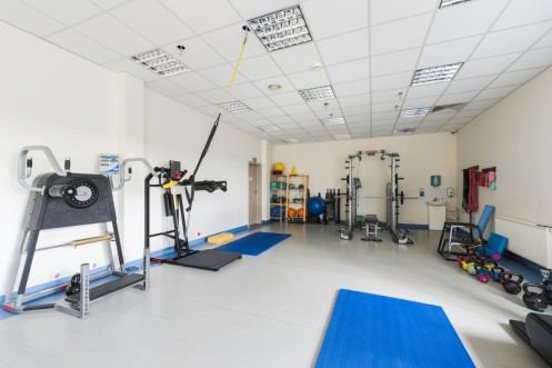Sala treningu funkcjonalnego z klatką do ćwiczeń, matami oraz sprzętem siłowym. 
